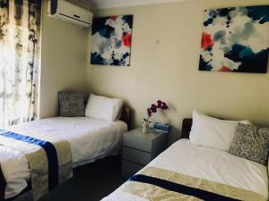 a bedroom with two beds and a window and paintings at Swan Valley Rest Cottage in Middle Swan