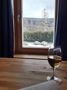a glass of wine sitting on a table in front of a window at Chata Brigit in Vrbno pod Pradědem