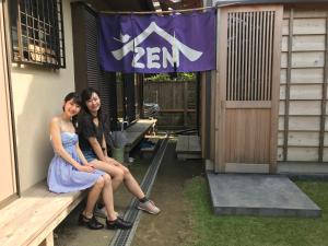 鐮倉的住宿－鎌倉澤傑旅館，两个年轻的女人坐在大楼前的长凳上