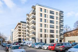 a large white building with cars parked in a parking lot at Bulwary Wislane P&O Serviced Apartments with AC in Warsaw