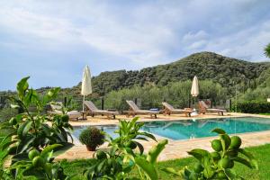 a pool with chairs and umbrellas next to a mountain at Villa Larna Corfu in Kavvadádes