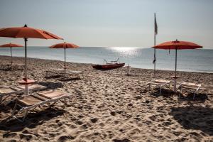 a beach with umbrellas and chairs and a boat at Masseria Macchia & Relais San Pio in Marina di Pisticci