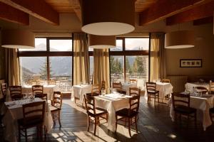 un restaurante con mesas y sillas blancas y ventanas grandes en Chaberton Lodge & Spa, en Sauze dʼOulx