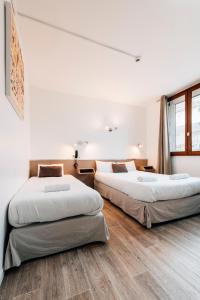 two beds in a room with white walls and wooden floors at Hôtel Alizé in Toulouse