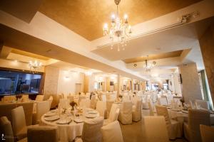 une salle de banquet avec des tables et des chaises blanches ainsi qu'un lustre dans l'établissement Hotel Ozana, à Bistriţa