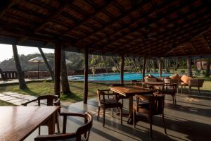 patio ze stołami i krzesłami oraz basenem w obiekcie Prainha Resort By The Sea w mieście Panaji