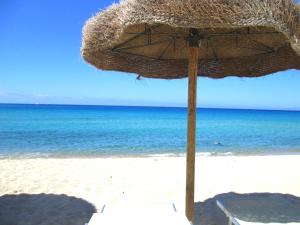 a straw umbrella on a beach with the ocean at Sardinia Yellow House in Solanas