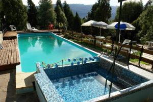 a large swimming pool with chairs and an umbrella at Cabañas del Faldeo Titos in El Bolsón