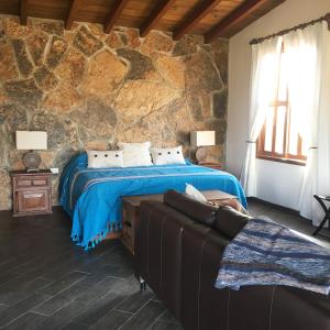 1 dormitorio con cama y pared de piedra en En'kanto Valle de Guadalupe, en San Marcos