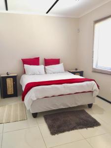 a white bedroom with a large bed with red pillows at Man Cave Suite in Swakopmund