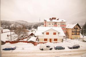a snow covered city with cars parked in front of a building at Apartament Happynest in Predeal