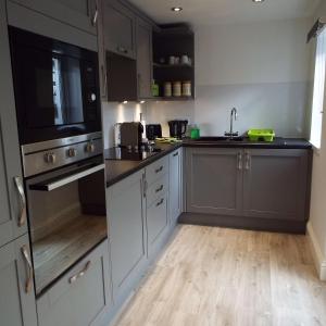 a kitchen with white cabinets and black appliances and wooden floors at Turner Cottage in Norham