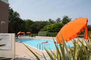 una piscina con ombrellone arancione e persone di Residenza Al Parco a Bibione