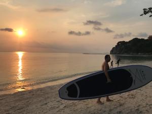 a man standing on the beach holding a surfboard at Sarikantang Resort & Spa, Koh Phangan in Haad Rin