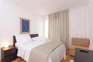 a white bedroom with a bed and a chair at Guesthouse Mate Ledic in Brela