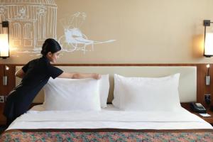 a woman putting pillows on a bed in a hotel room at Swiss-Belhotel Airport Jakarta in Tangerang