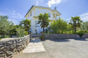a white building with a stone wall and palm trees at Apartments Ljubica in Malinska