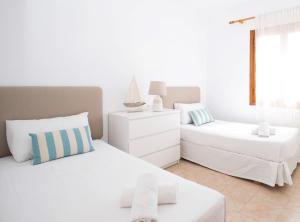 a white bedroom with two beds and a window at Villa Margarita in Es Mercadal