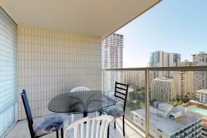 einen Balkon mit einem Glastisch und Stühlen sowie eine Stadt in der Unterkunft Island Colony Suites in Honolulu