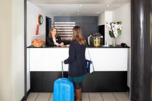 uma mulher parada num balcão com uma mala azul em Aparthotel Adagio Access La Défense - Place Charras em Courbevoie