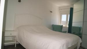 a bedroom with a white bed and two green chairs at Apartamento Próximo da Praia in Luz