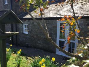 a stone house with a white door and flowers at The Snug @ Corry Cottage in Haltwhistle