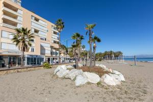 a sandy beach with palm trees and a building at La Roca Chica in Torremolinos