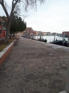 a stone walkway next to a river with a tree at Comfort Murano room in Murano +1 photo