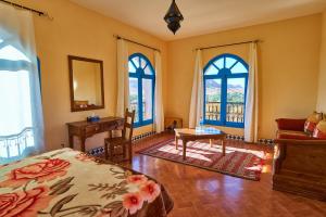 a bedroom with a bed and a desk and windows at Maison D'hotes Sahara in Aoufous