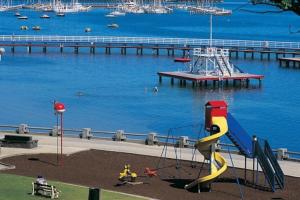 a playground with a slide in front of a body of water at The Beach House Apartment in Geelong