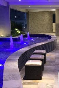 a swimming pool with benches and a fountain in a building at Classe e Conforto in Praia Grande