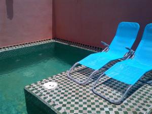 a swimming pool with two blue chairs in the water at Riad Lila in Marrakesh