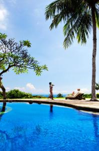 a swimming pool with palm trees and a person sitting on a beach at The Damai in Lovina
