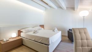 a white bedroom with a bed and a chair at Scicli Albergo Diffuso in Scicli