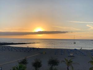 a sunset over a beach with chairs and the ocean at Torres del Sol Playa de Las Vistas FREE WIFI in Playa de las Americas