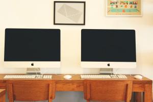 two computer monitors sitting on top of a wooden desk at Bloomrooms @ Link Road in New Delhi