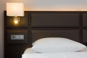 a bed with a white pillow and a light above it at Wyndham Köln in Cologne