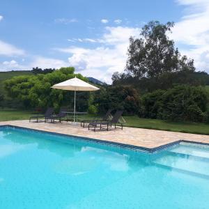 a swimming pool with two chairs and an umbrella at Chácara Leolud in Socorro
