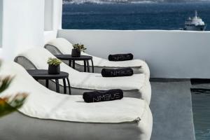 three white chairs with pillows on them in a room with the ocean at Nimbus Mykonos in Agios Stefanos