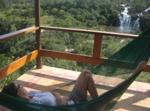 a woman laying in a hammock in front of a waterfall at Pousada Cachoeira Poço Encantado in Alto Paraíso de Goiás