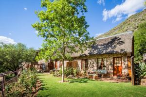 an old stone house with a tree in the yard at De Poort Country Lodge in Oudtshoorn