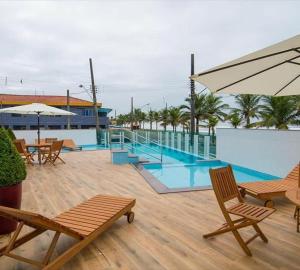 a swimming pool with chairs and an umbrella at Edifício Copacabana frente para mar in Mongaguá