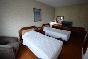 a hotel room with two beds and a chair and a mirror at Caravelle Palace Hotel in Curitiba