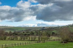 a field with a fence and animals in the distance at The Dovecote, Stoke Farthing Courtyard in Broad Chalke