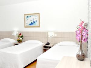 a hotel room with two beds and a vase of flowers at Caravelle Palace Hotel in Curitiba