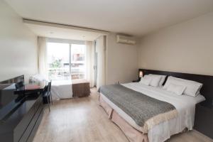 1 dormitorio con 2 camas, escritorio y ventana en 27 Suites Hotel, en Montevideo