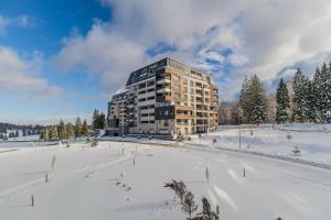 un edificio en un campo cubierto de nieve con árboles en Charming 2-Bedroom, Silver Mountain, A Building, en Poiana Brasov