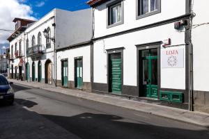 a white building with green doors on a street at Casa Caió in Ribeira Grande