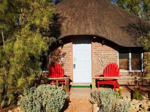 two red chairs sitting in front of a building with a thatch roof at Terra Rouge Guestfarm & Sonstraal Farmhouse in Koës