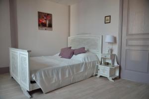 a white bedroom with a white bed with purple pillows at Le Tacot in Pont-de-Poitte